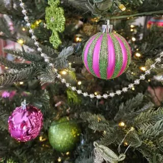 Closeup of pink and green glitter ornaments on a christmas tree.